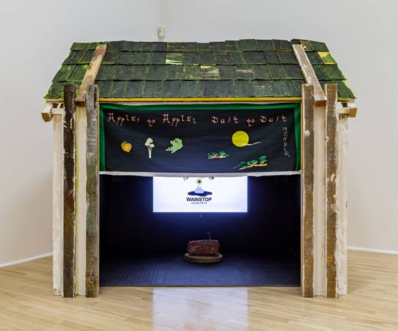 Art installation of a wooden structure with a TV monitor inside, showing the Wainstop logo.